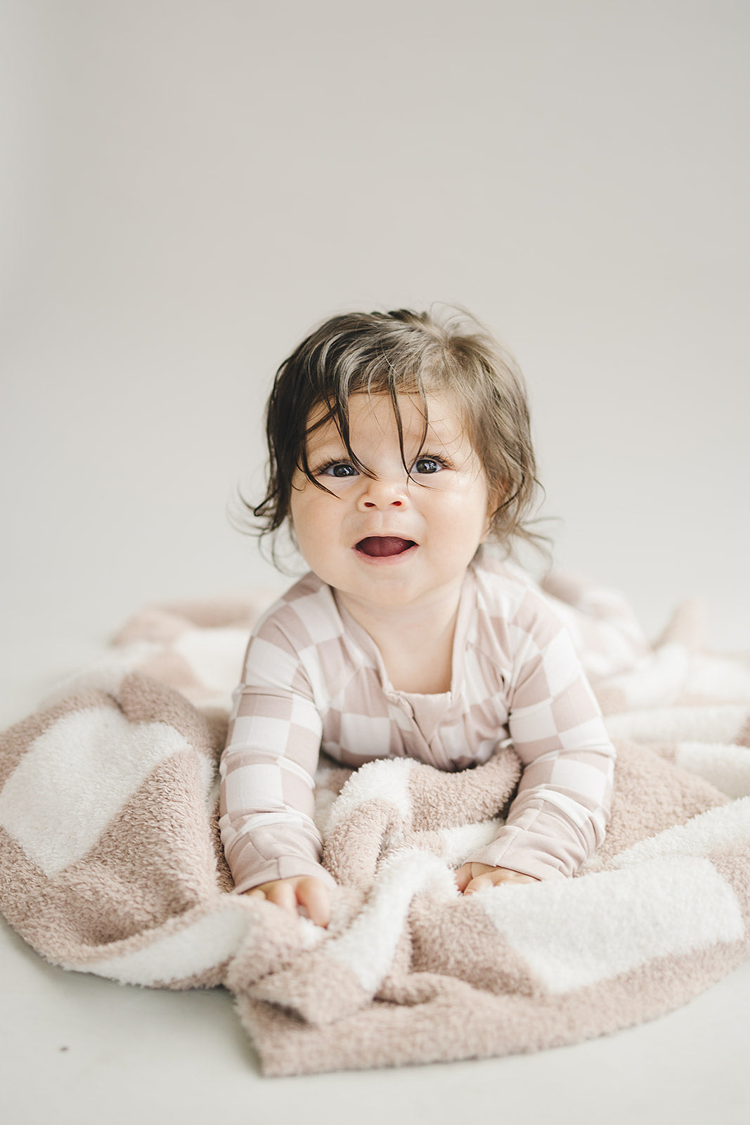 smiling baby resting on plush checkered blanket in light neutral clothing