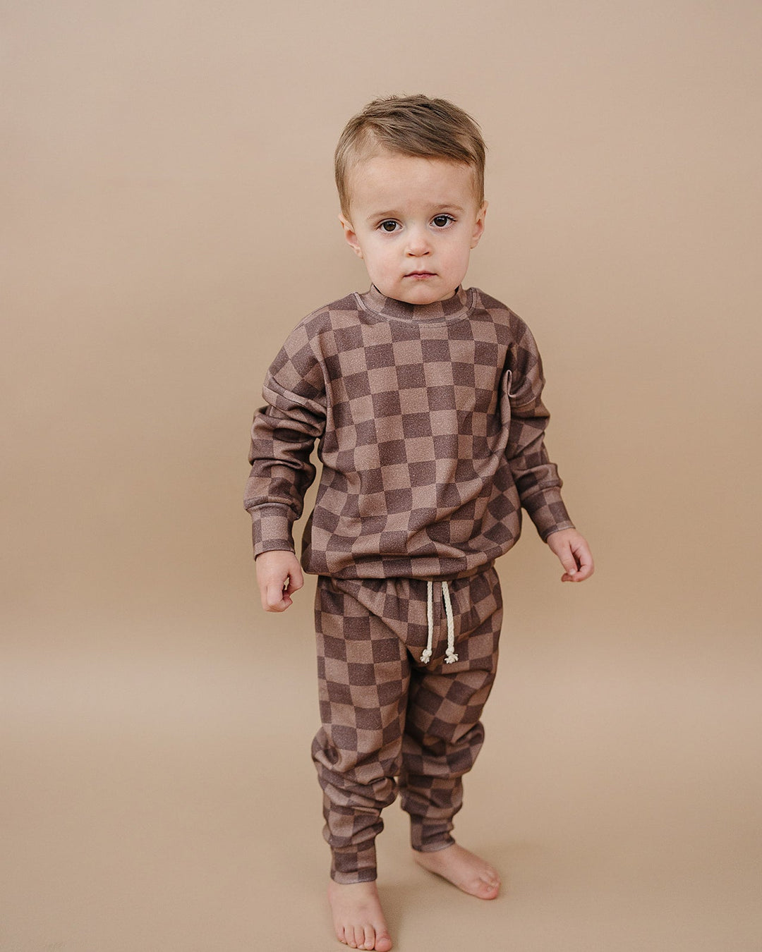 baby wearing a checkered smiley lounge set in neutral latte tones sitting on a cozy blanket