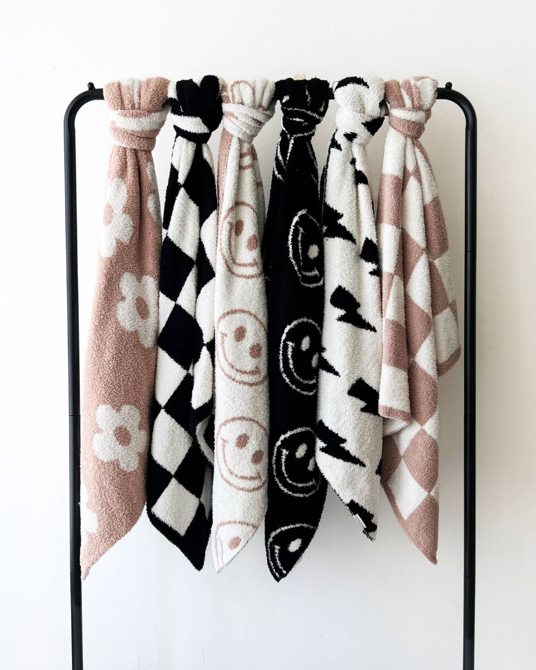 plush baby blankets with smiley and checkered patterns hanging on a black rack