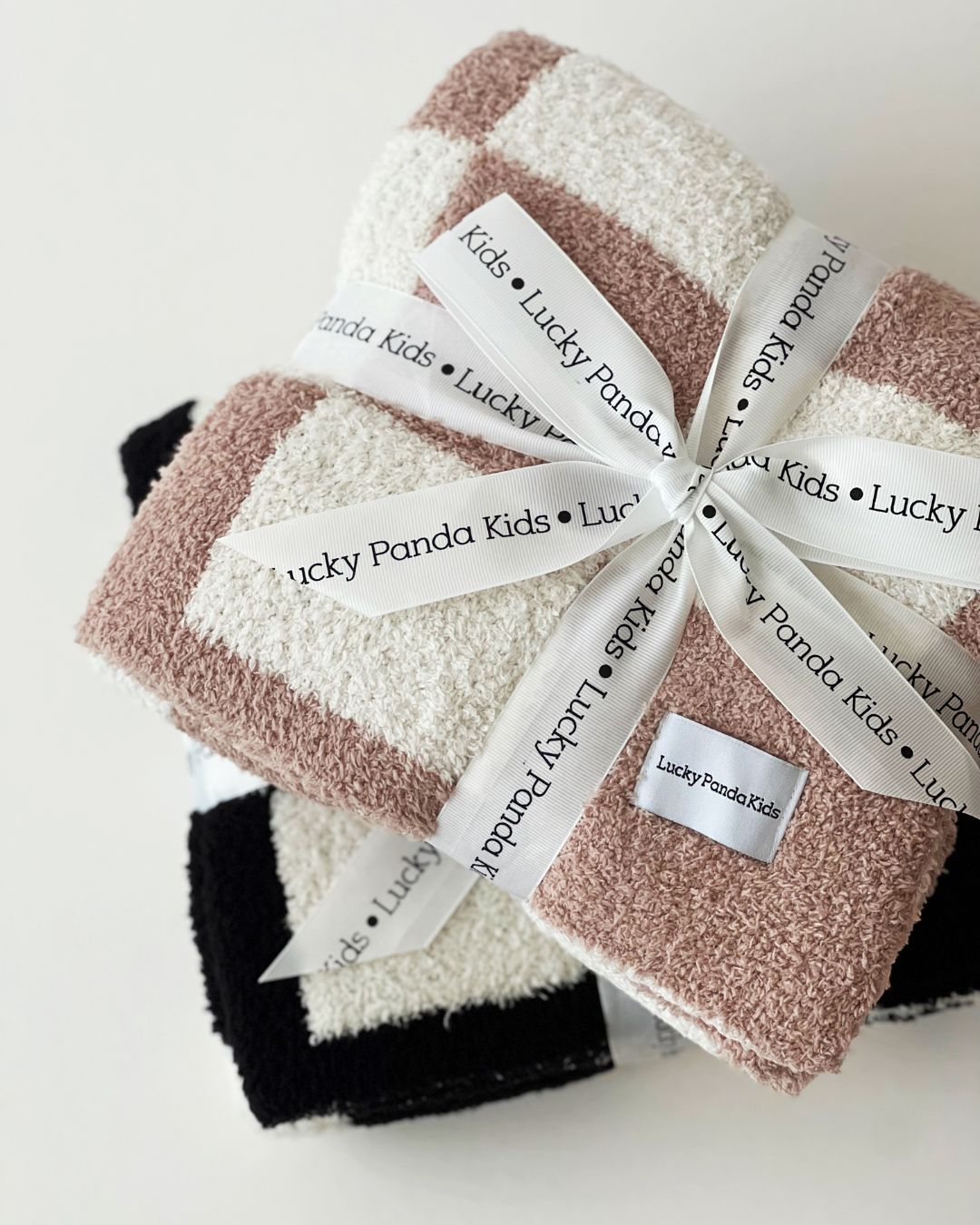 folded plush baby blankets wrapped with Lucky Panda Kids ribbon in neutral colors