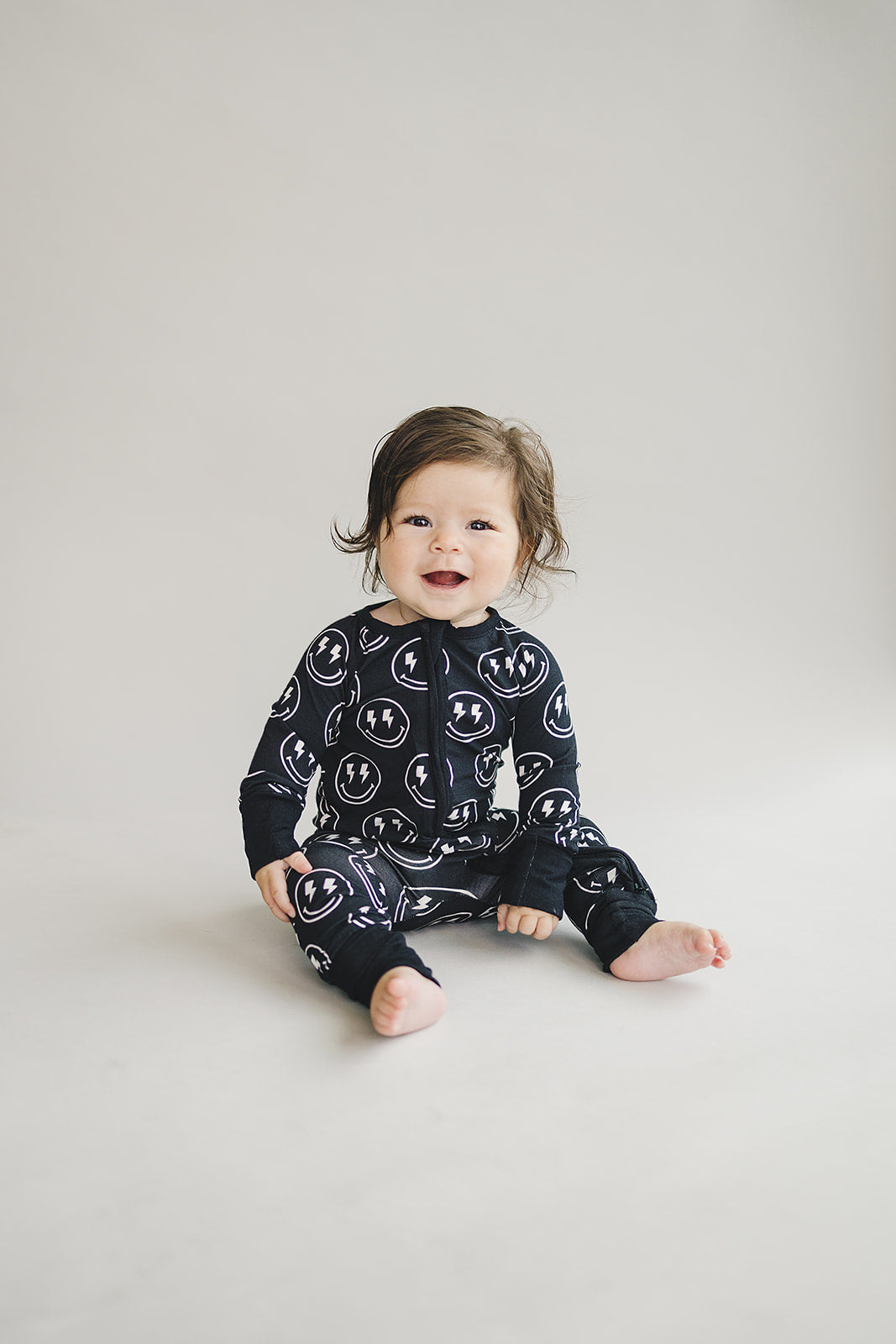 Seated little one wearing the Electric Smiley Bamboo Zip Romper