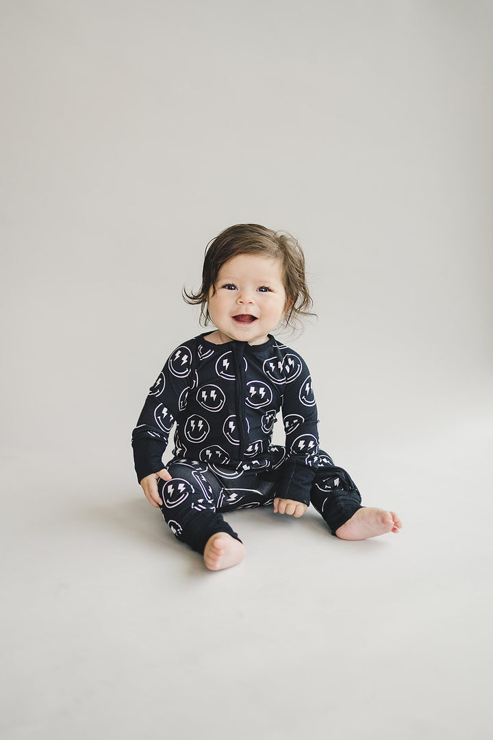 Seated little one wearing the Electric Smiley Bamboo Zip Romper