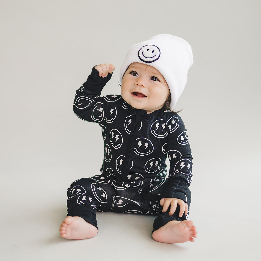 Baby wearing the Electric Smiley Bamboo Zip Romper with coordinating smiley beanie