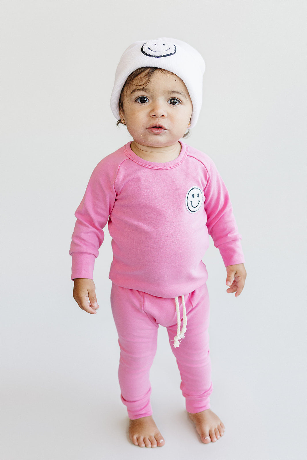 Baby wearing a pink outfit with smiley face design on a white background