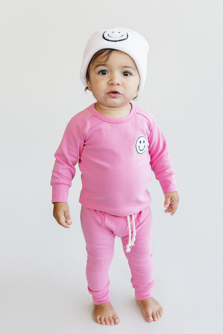 Baby wearing a pink outfit with smiley face design on a white background