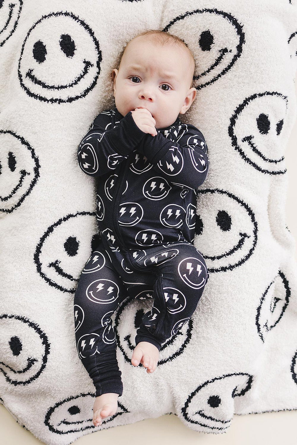 Baby wearing the Electric Smiley Bamboo Zip Romper on a smiley face blanket