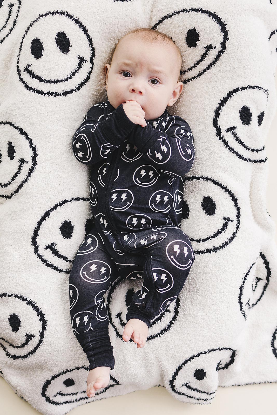 Baby wearing the Electric Smiley Bamboo Zip Romper on a smiley face blanket