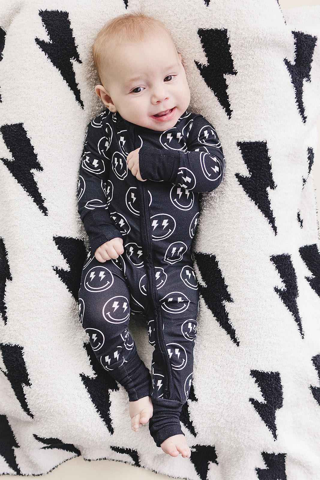 Baby relaxing in the Electric Smiley Bamboo Zip Romper on a lightning print blanket