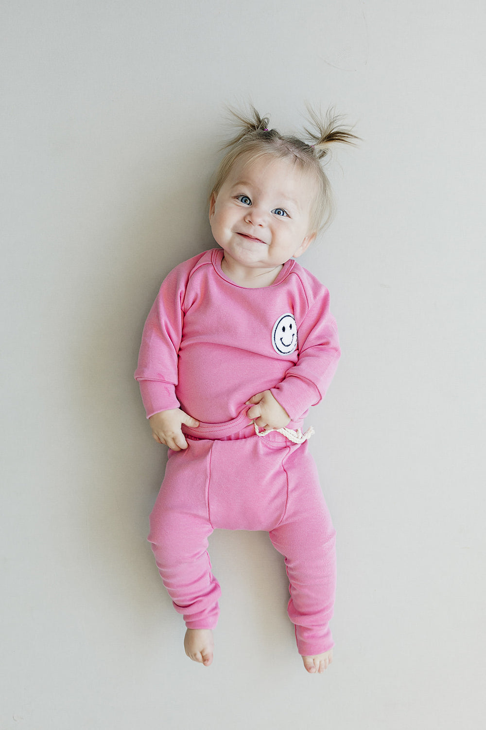 Child wearing a pink outfit with a smiley face design on a plain background