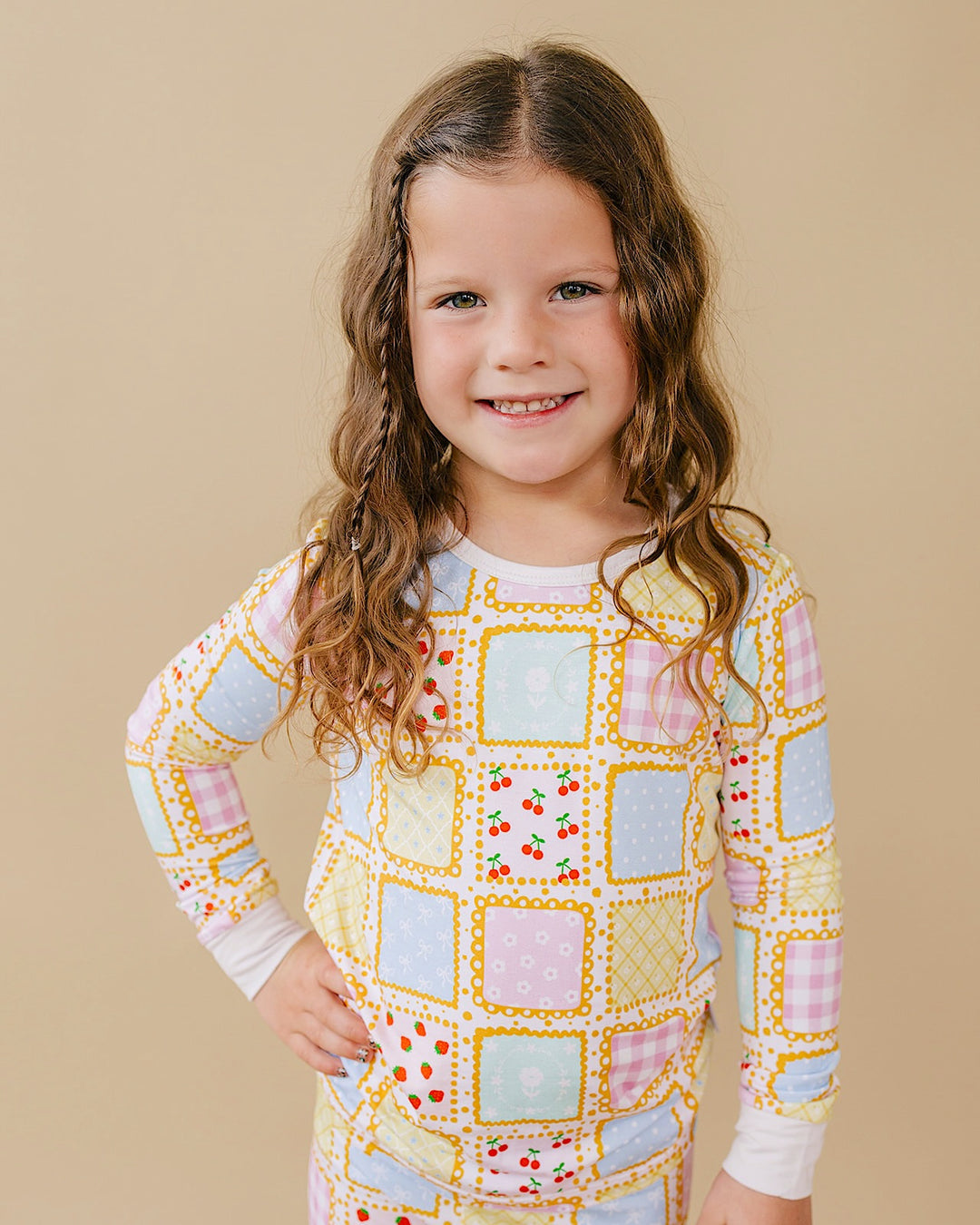 Smiling child wearing Sweet Patchwork pajamas with pastel squares, strawberry prints, yellow borders and white cuffs.