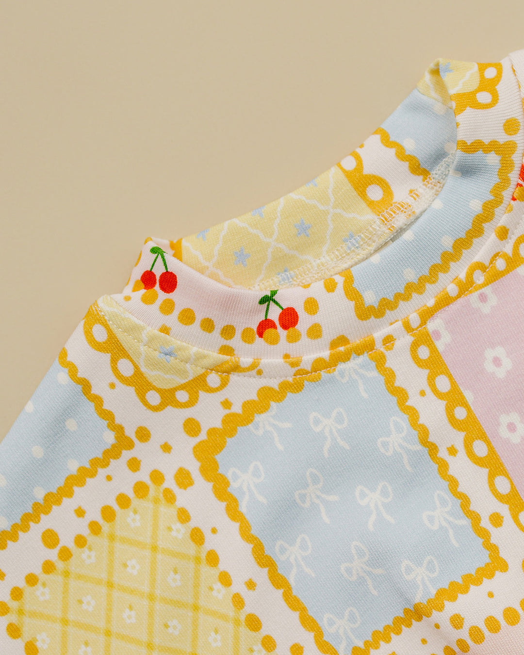 Detail of the Sweet Patchwork top showing the neckline, yellow borders, pastel checks and floral squares.