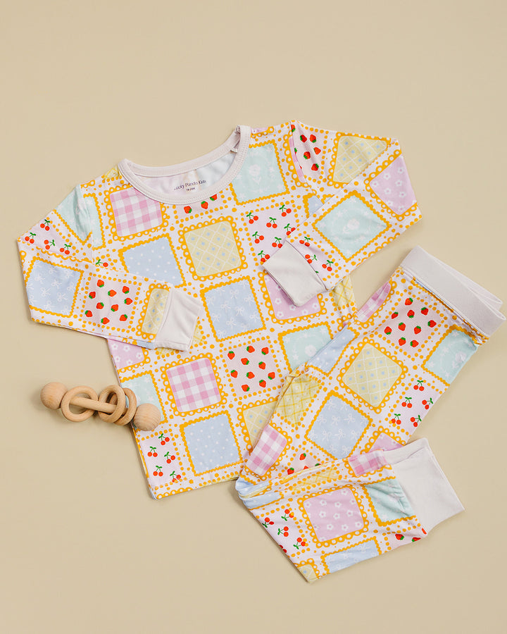 Sweet Patchwork long sleeve pajama top and matching pants laid flat beside a wooden toy.
