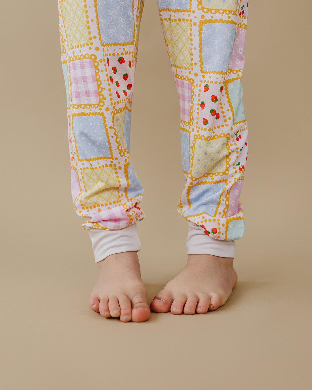 Close up of Sweet Patchwork pajama pants showing pastel printed squares, white ankle cuffs and bare feet.