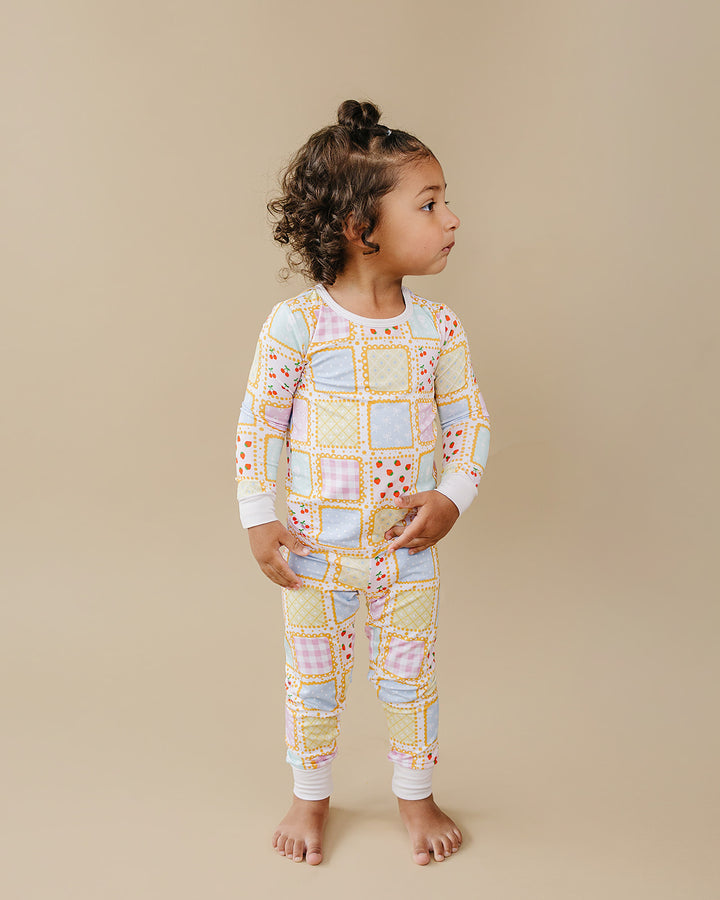 Toddler looking to the side while wearing the Sweet Patchwork pajama set with yellow borders and white cuffs.