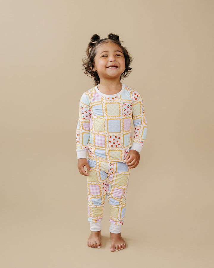 Smiling toddler standing barefoot in Sweet Patchwork two piece pajamas with pastel prints and white trim.