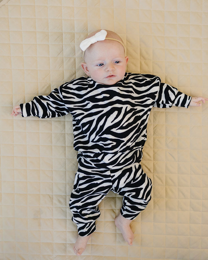 Baby wearing the Zebra Jogger Set while relaxing on a quilted blanket