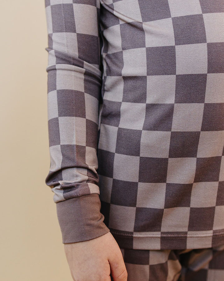 A close-up of a person wearing a long-sleeve top with a gray and white checkerboard pattern, showing the sleeve cuff and part of the torso against a plain beige background.