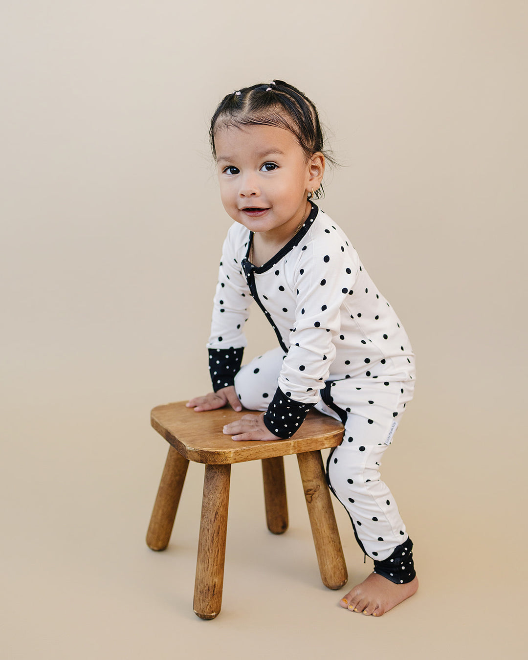 Little one wearing the Classic Polka Bamboo Zip Romper beside a wooden stool