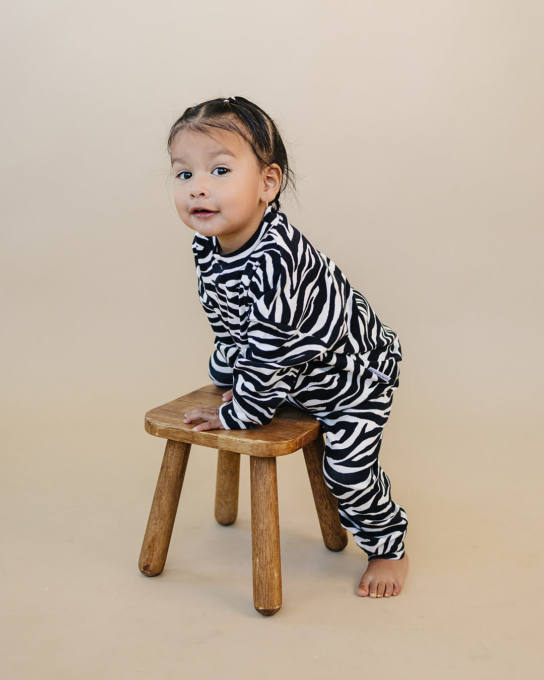 Little one wearing the Zebra Jogger Set beside a wooden stool