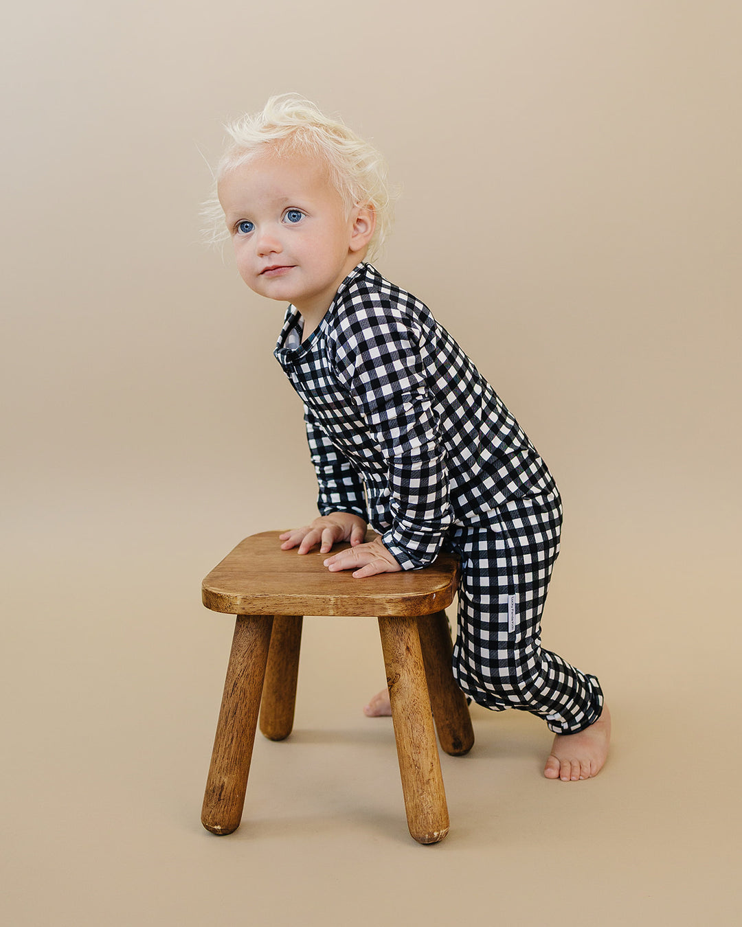 Little one wearing the Black Gingham Bamboo Zip Romper beside a wooden stool