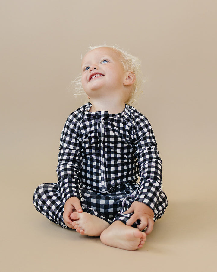 Seated little one wearing the Black Gingham Bamboo Zip Romper