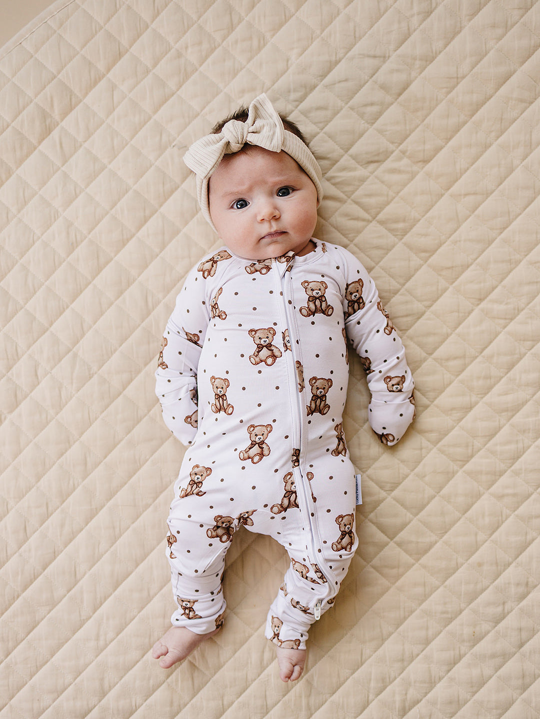 Baby lying on a cream quilted mat in the Cute Bear bamboo zip romper.