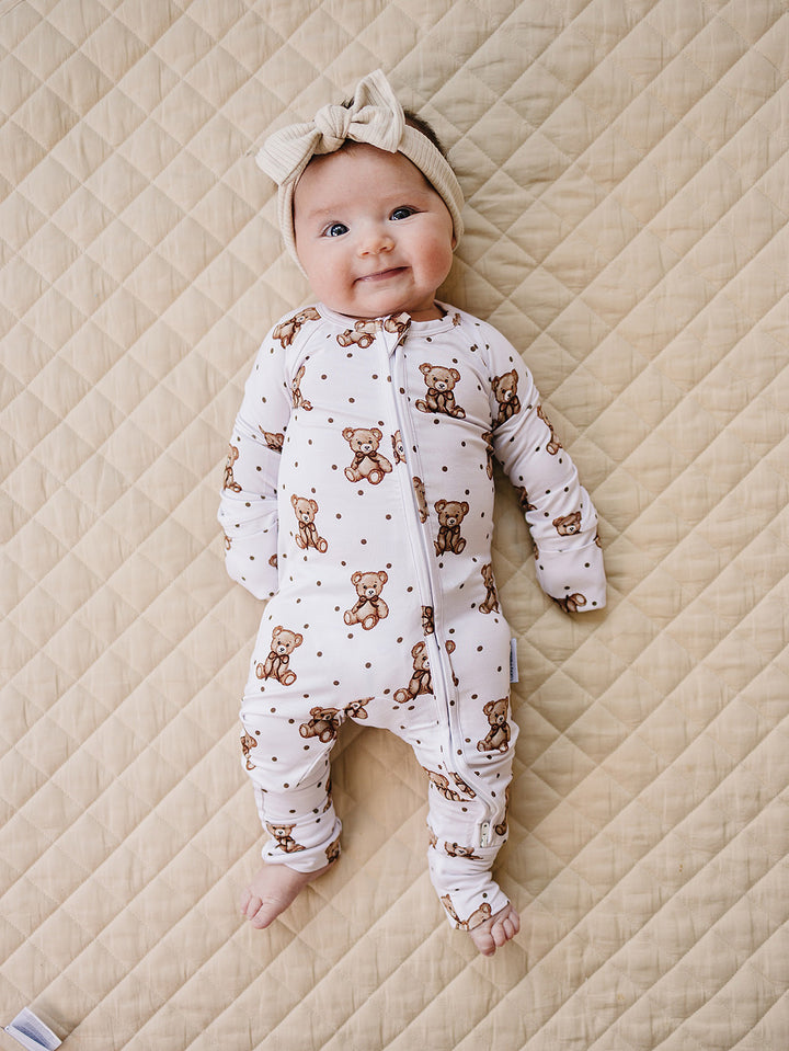 Smiling baby wearing the white Cute Bear bamboo romper and matching bow headband.