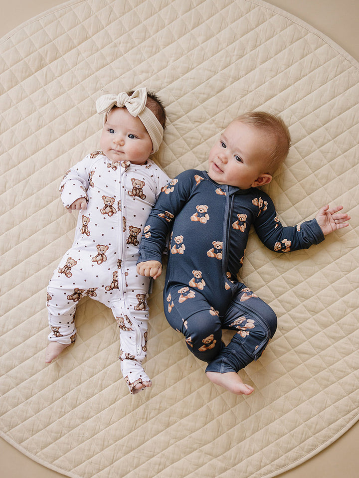 Two babies wearing coordinating Bear Vibes bamboo zip rompers on a quilted mat.