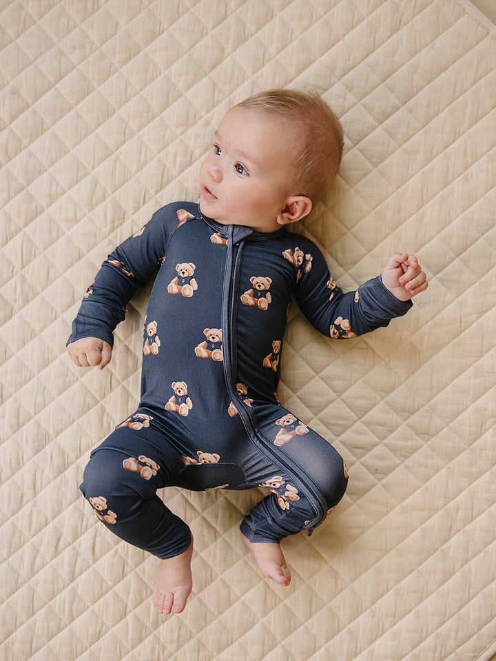 Baby lying on a cream quilted mat in the dark charcoal teddy bear-print romper.