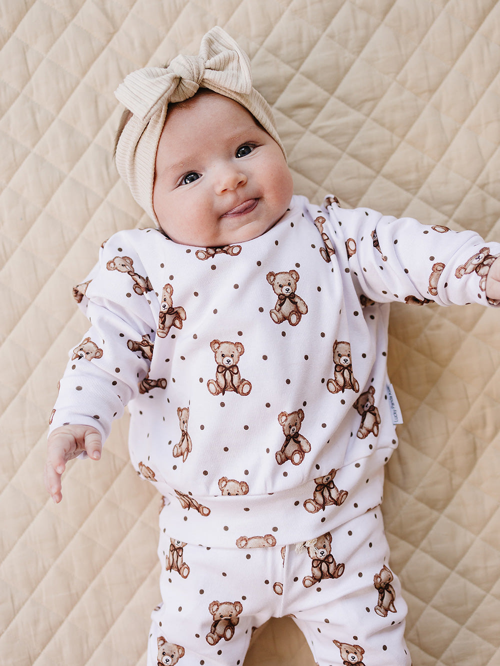 Baby lying on a cream quilted mat in the Cute Bear two-piece jogger set.
