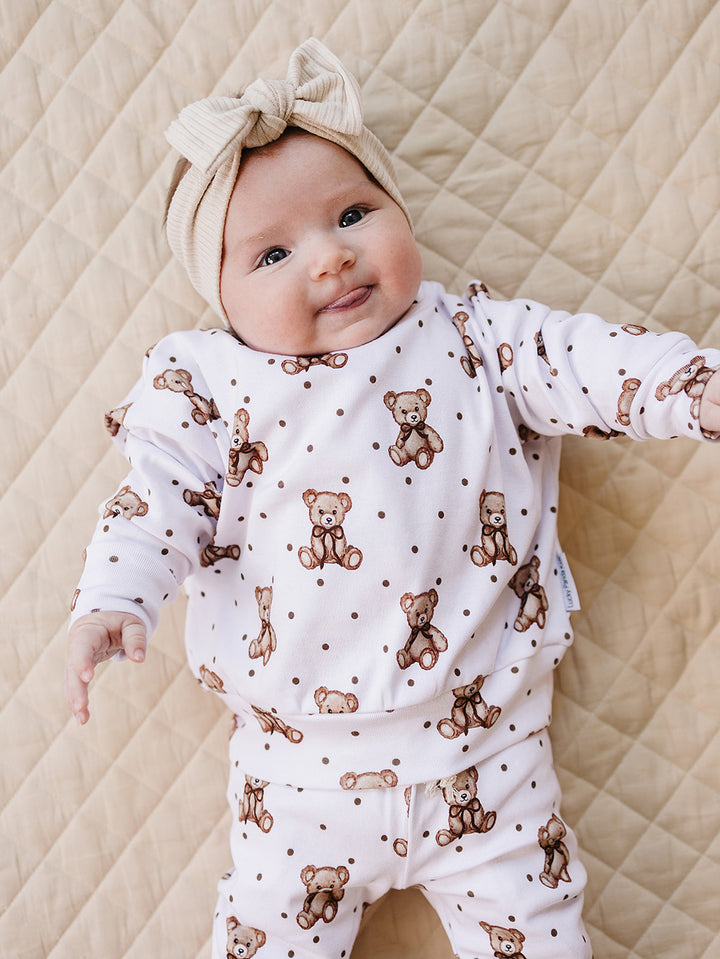 Baby lying on a cream quilted mat in the Cute Bear two-piece jogger set.
