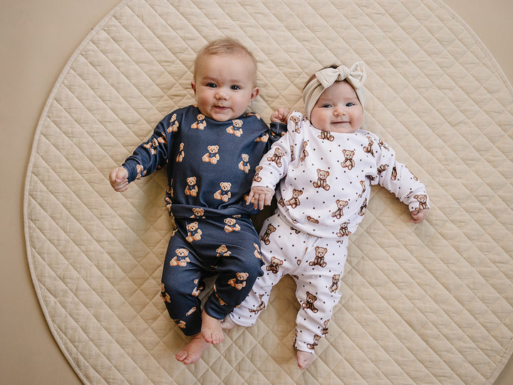 Two babies wearing coordinating dark charcoal and white bear-print outfits on a quilted mat.

