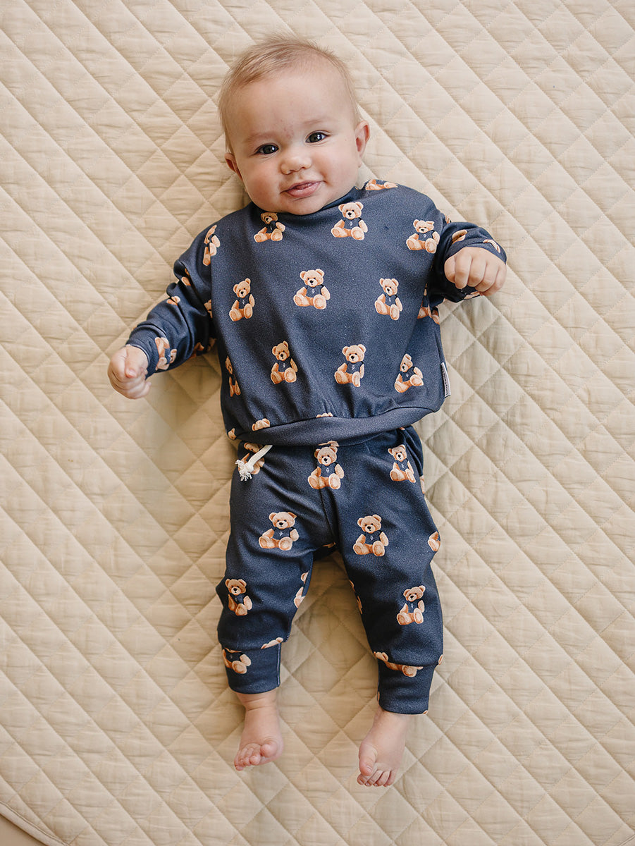 Baby wearing the Bear Vibes long-sleeve top and matching jogger pants on a cream quilted mat.