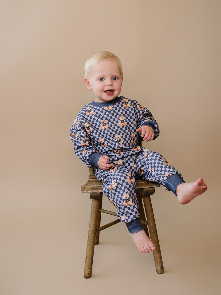 Baby sitting on a wooden stool in the blue checkered bear-print jogger set.
