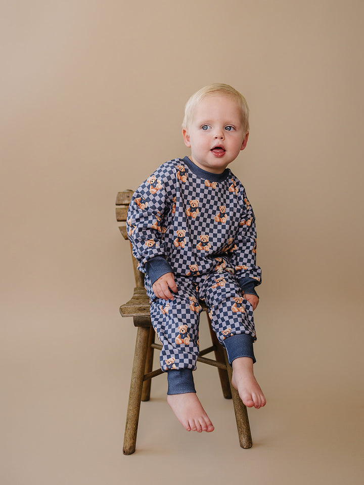 Baby sitting on a wooden stool wearing the Checkered Bear Vibes two-piece outfit.