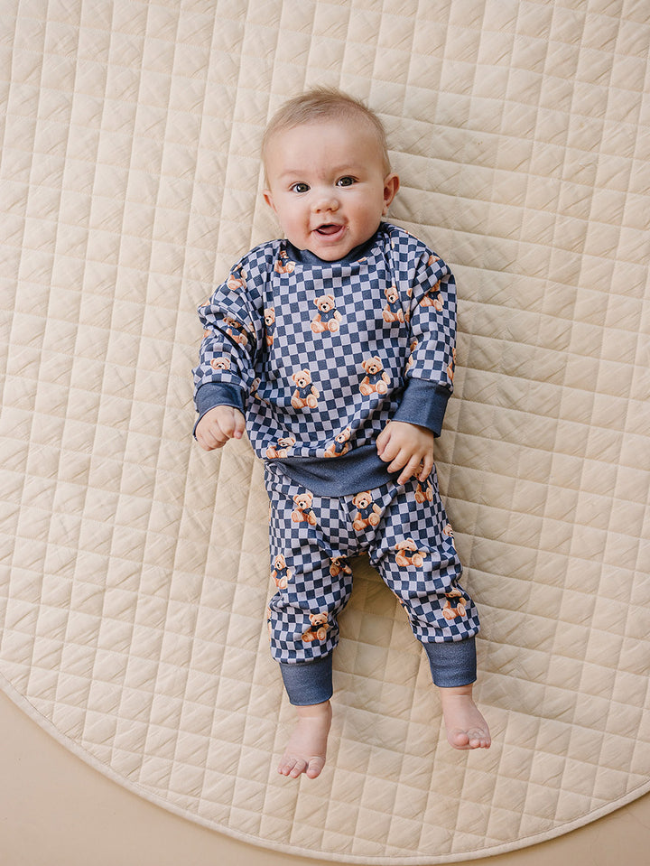 Baby wearing the Checkered Bear Vibes jogger set while lying on a cream quilted mat.