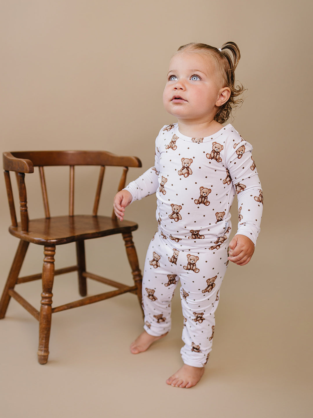 Toddler standing beside a wooden chair in the Cute Bear bamboo two-piece outfit.