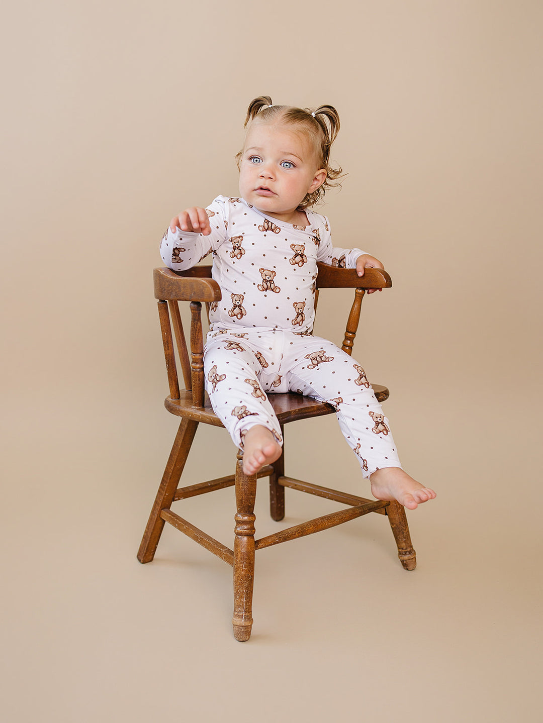 Toddler seated sideways in the white teddy bear-print top and matching pants.