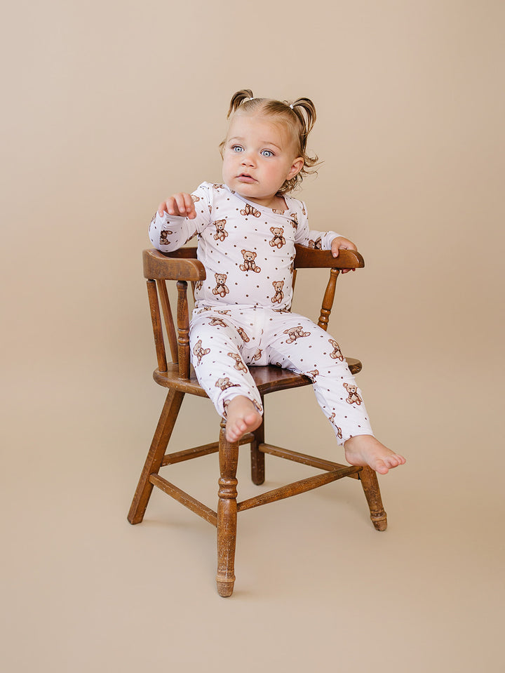 Toddler seated sideways in the white teddy bear-print top and matching pants.