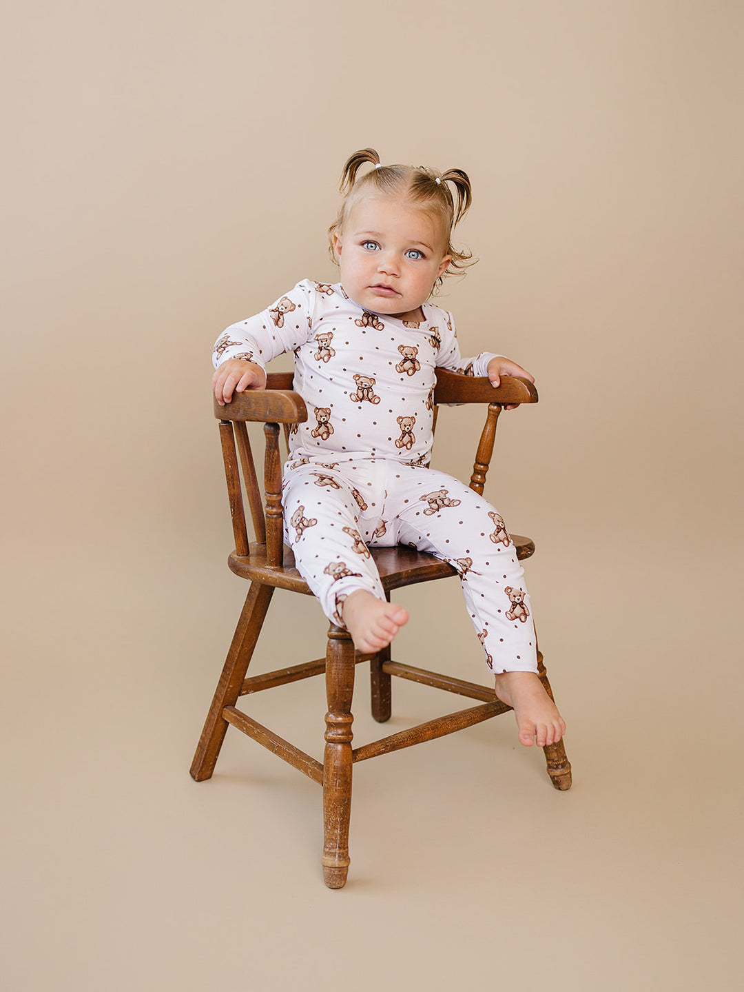 Smiling toddler wearing the Cute Bear two-piece bamboo set on a wooden chair.