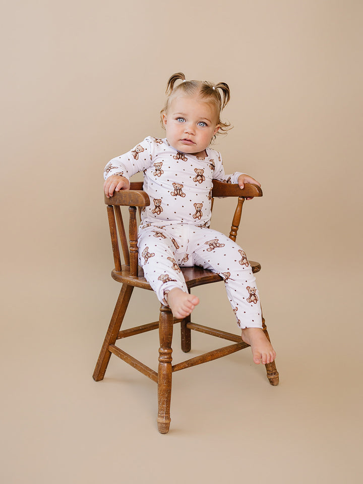 Smiling toddler wearing the Cute Bear two-piece bamboo set on a wooden chair.