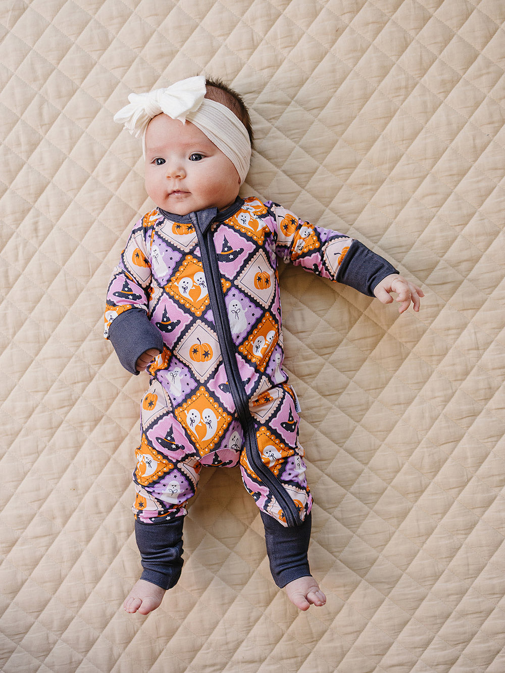 Baby lying on a quilted blanket in the Ghost Whimsy bamboo romper with one arm raised.
