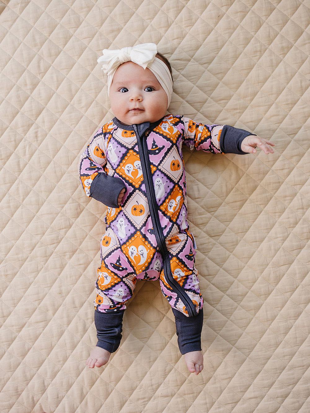 Baby wearing the Ghost Whimsy bamboo romper and a bow headband on a quilted blanket.