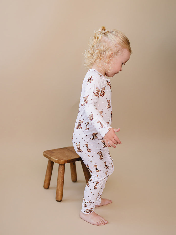 Toddler walking beside a wooden stool in the white cute bear-print romper.