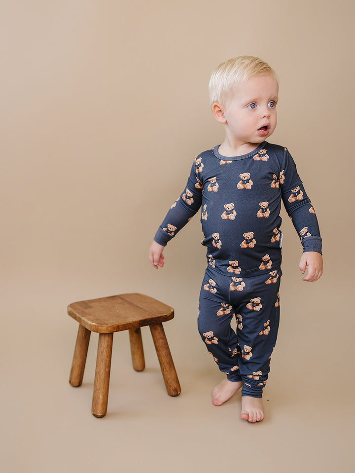Toddler walking in the dark charcoal Bear Vibes bamboo two-piece set beside a wooden stool.