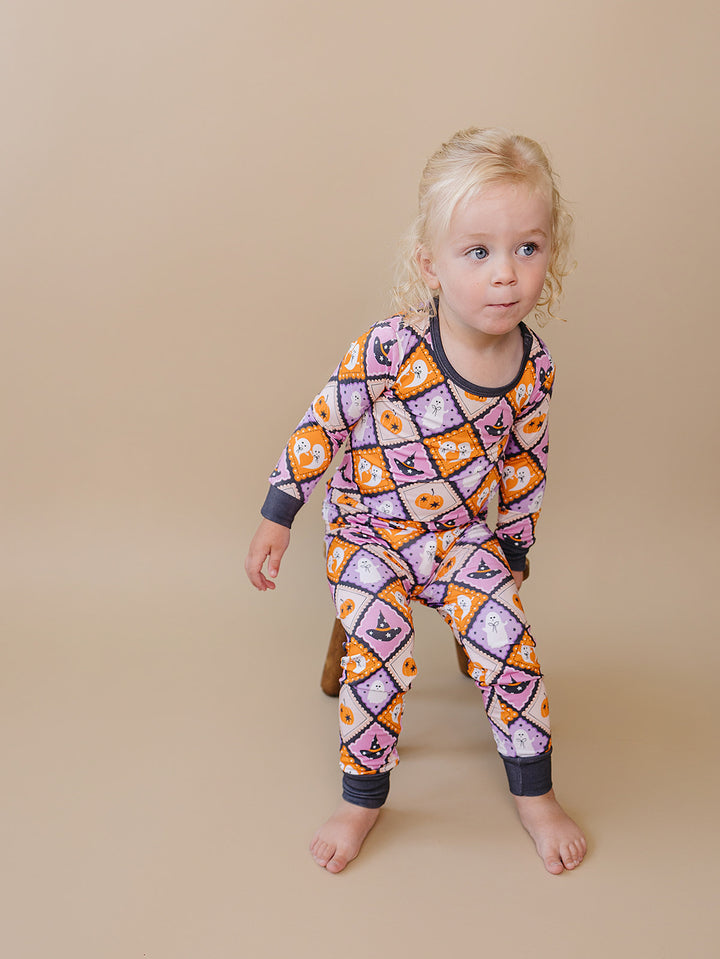 Toddler standing near a wooden stool in the purple and orange Halloween pajama set.