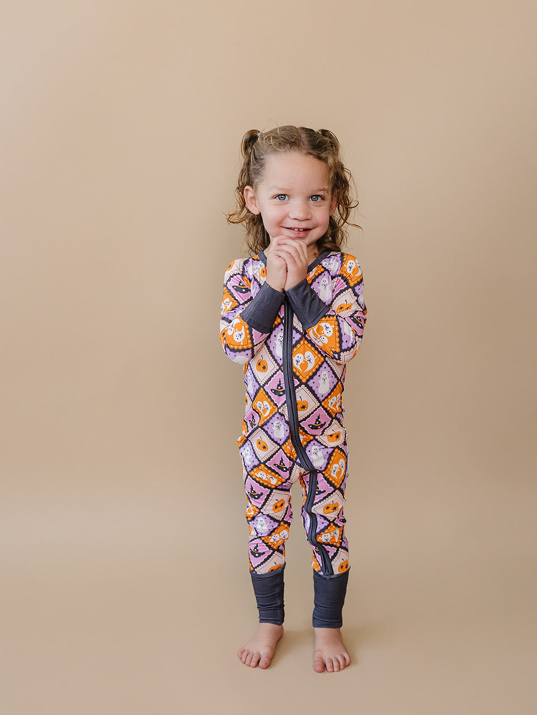 Toddler girl modeling the orange, lavender, and cream Ghost Whimsy Bamboo Zip Romper.