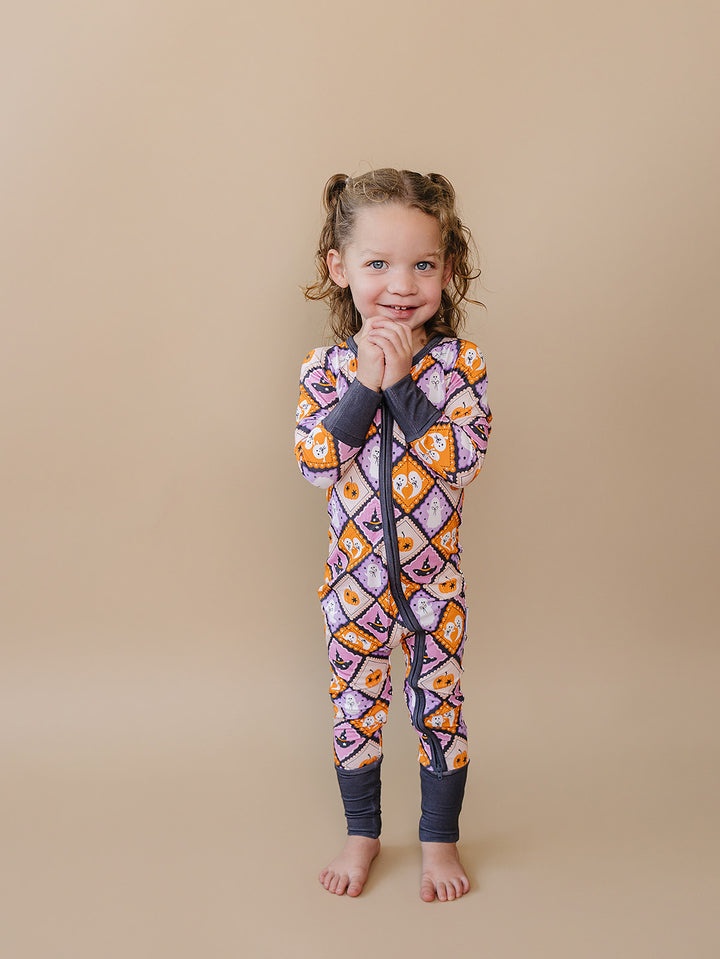 Toddler girl modeling the orange, lavender, and cream Ghost Whimsy Bamboo Zip Romper.