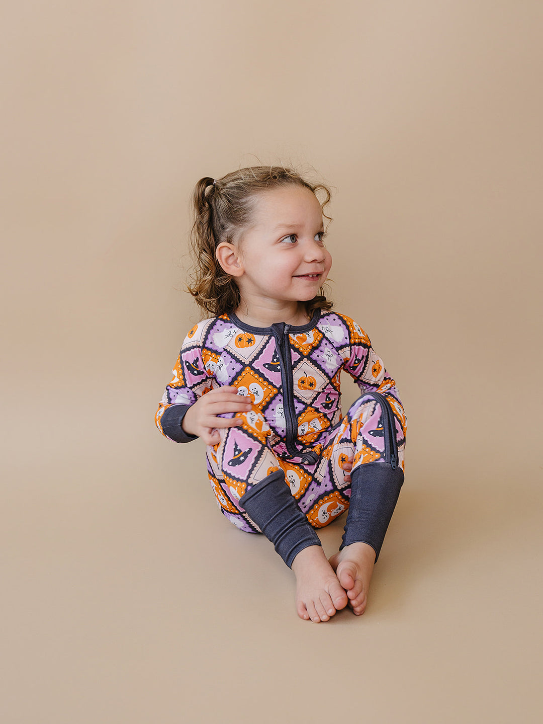 Toddler girl sitting and smiling in the Ghost Whimsy Halloween bamboo romper.