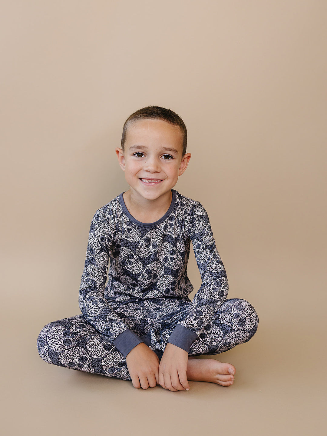 Child sitting cross-legged in the grey Leopard Skull Halloween Bamboo Pajama Set.